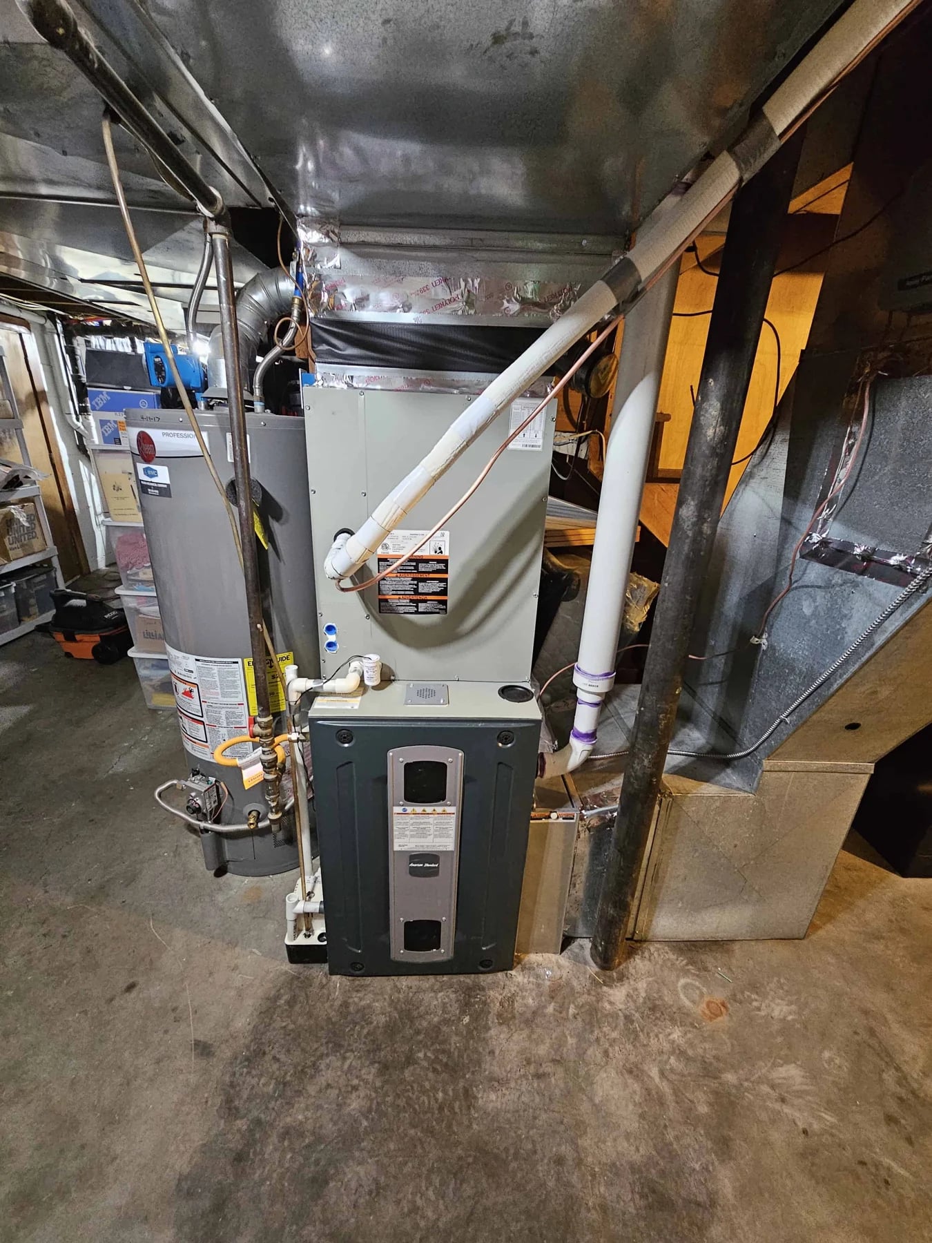 A basement furnace under sheet metal ductwork, next to a gas water heater