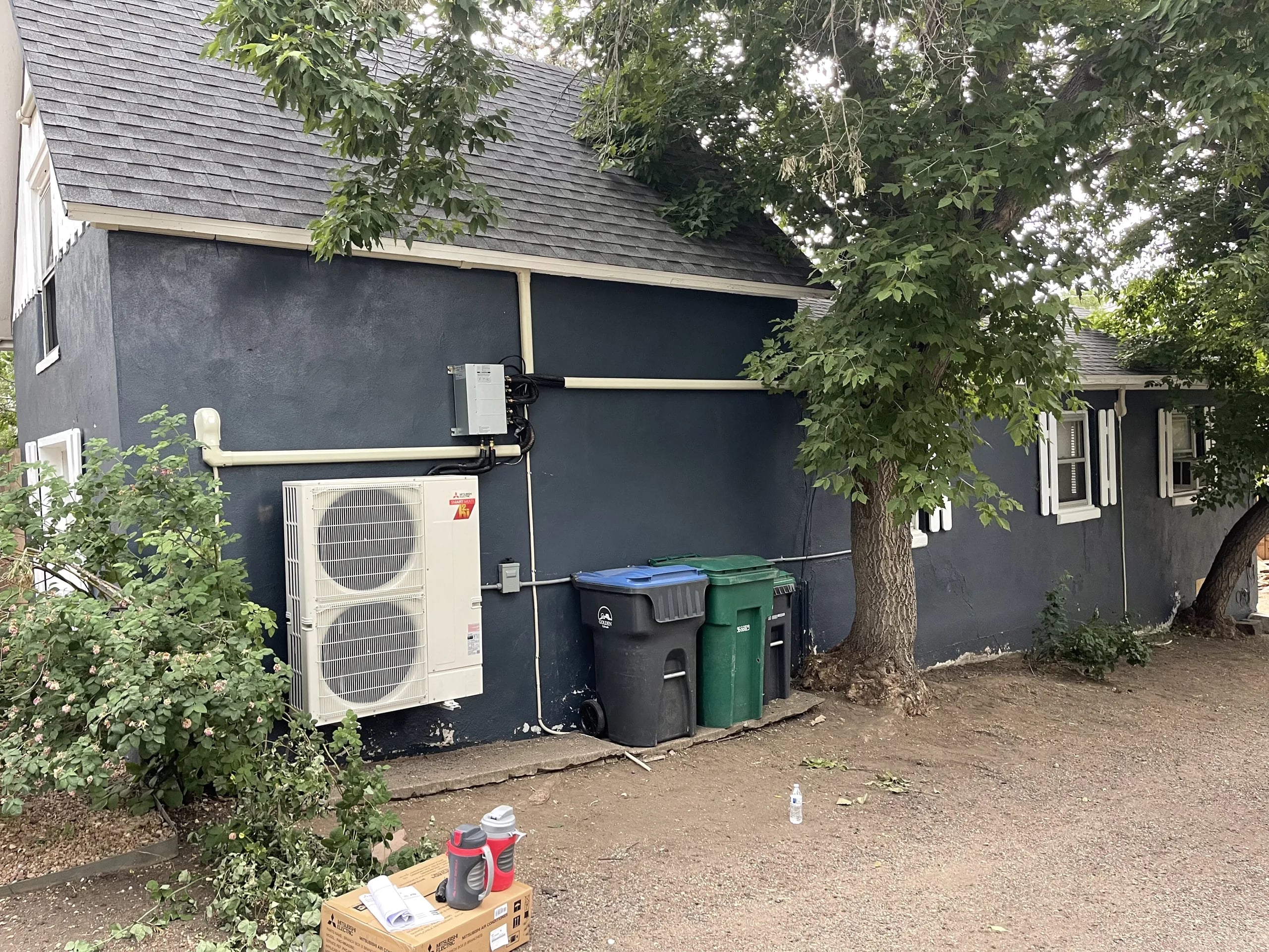Two-fan outdoor unit on a dark gray stucco wall, with a covered line set and a disconnect above it