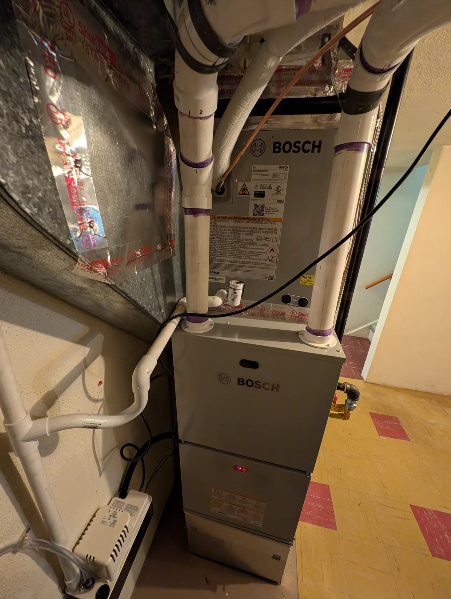 A Bosch furnace with a cased coil on top, white PVC vent pipes and a condensate pump
