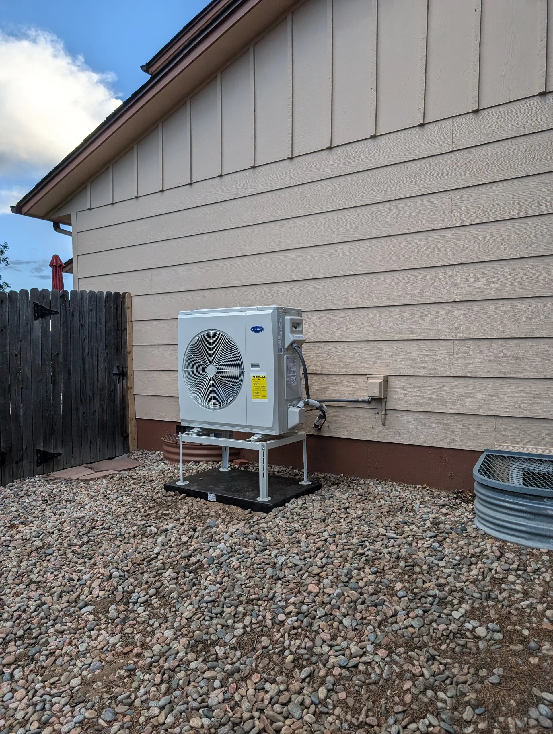 A compact Carrier heat pump on a stand in gravel beside beige siding