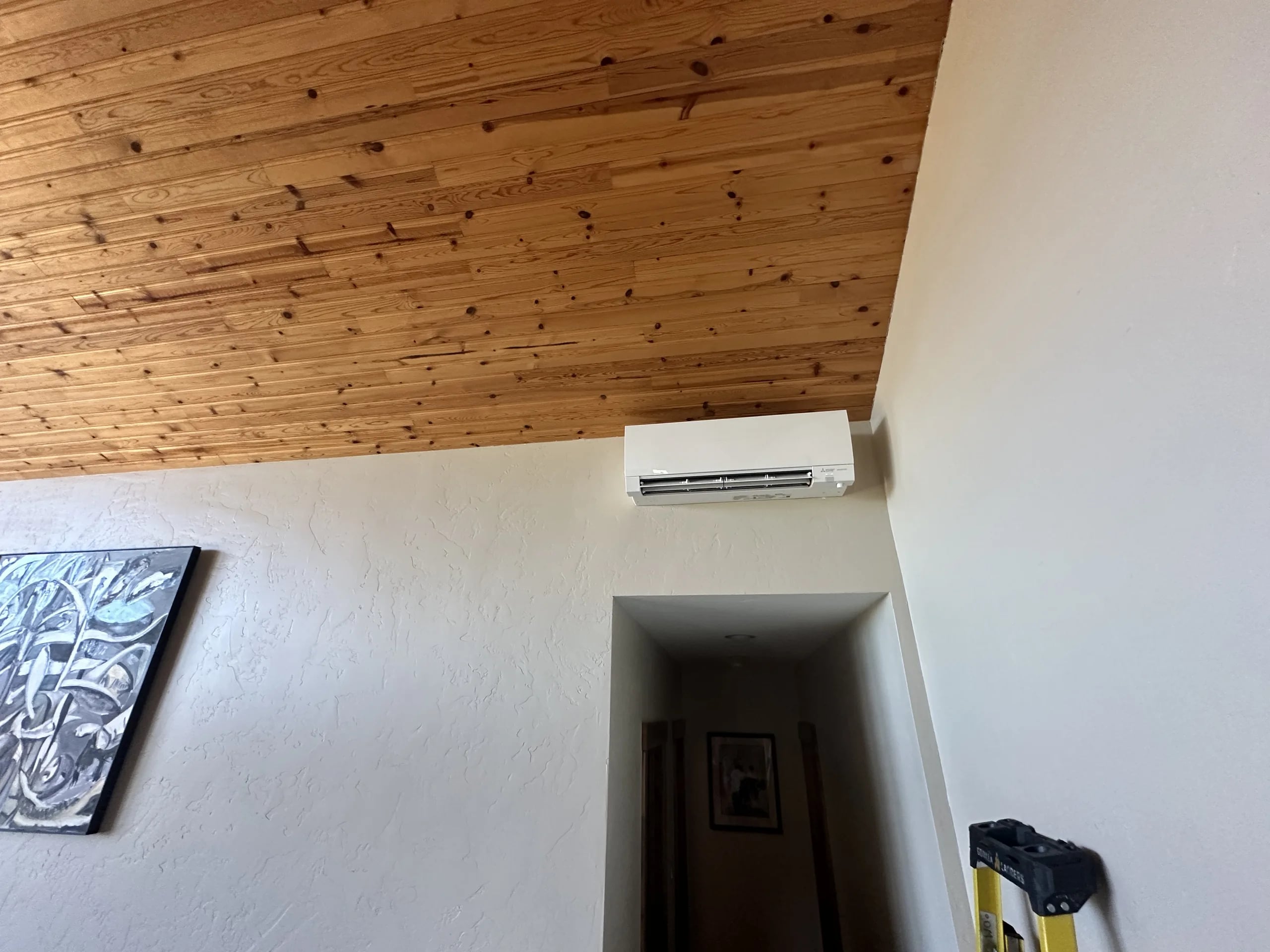 A white ductless wall head under a tongue-and-groove wood ceiling, above a hallway opening
