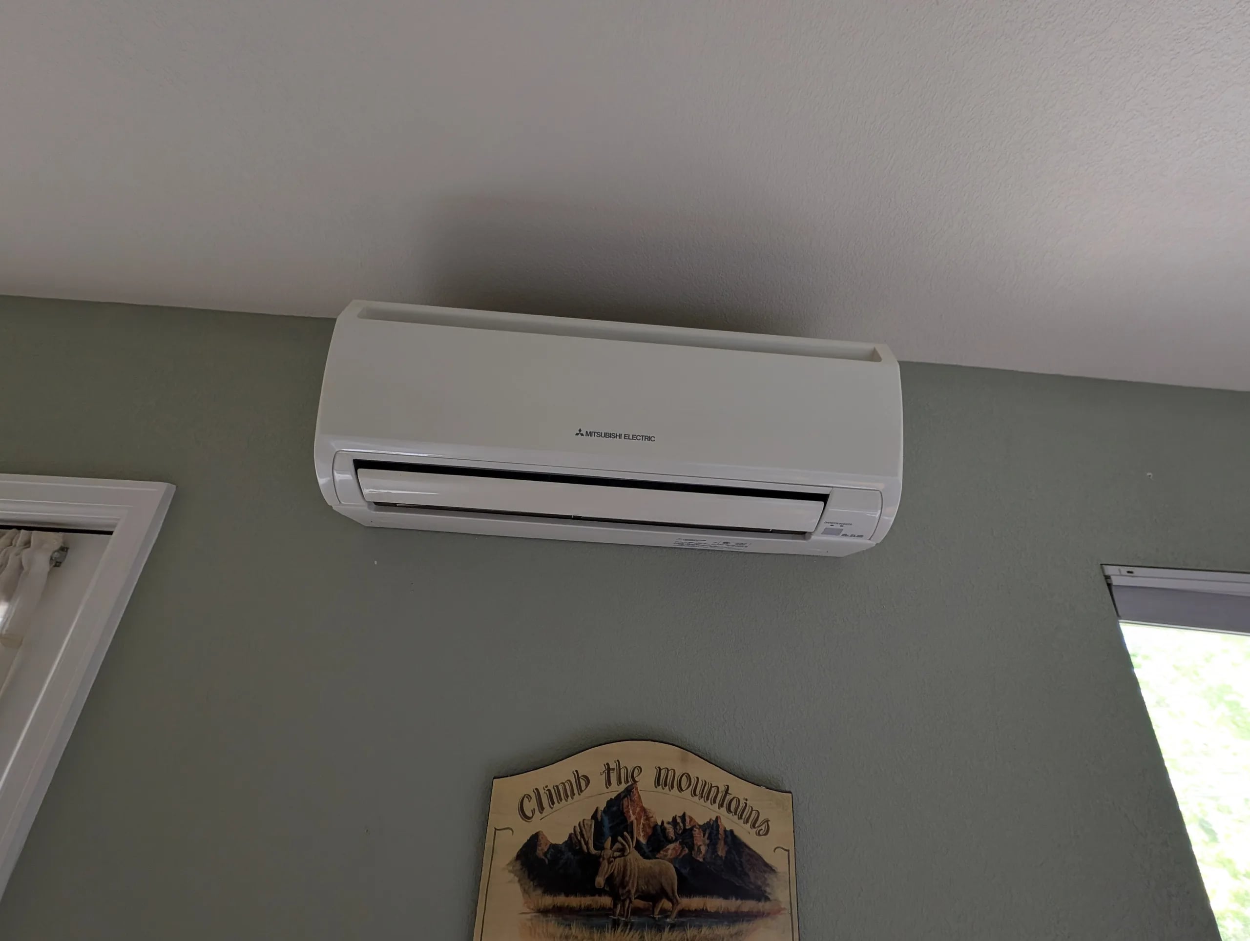 A white ductless wall head on a sage green wall above a small wooden mountain sign