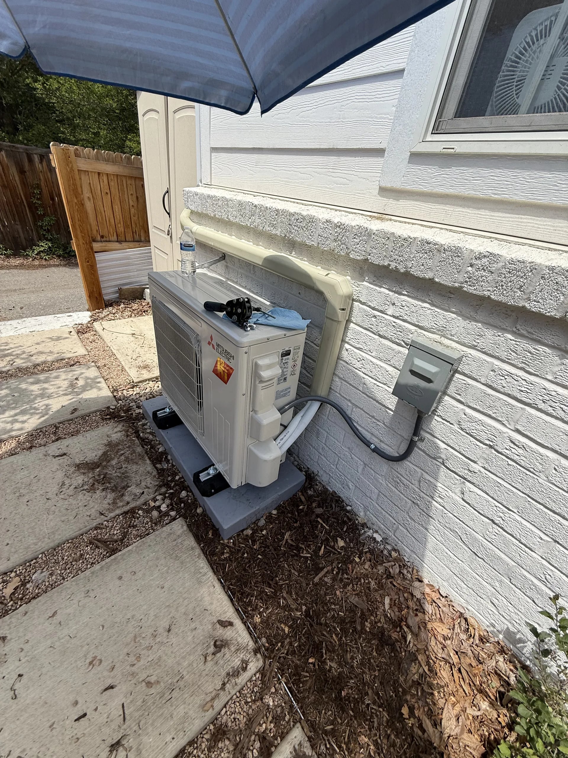 A Mitsubishi outdoor unit beside white painted brick, with a line set cover running to it