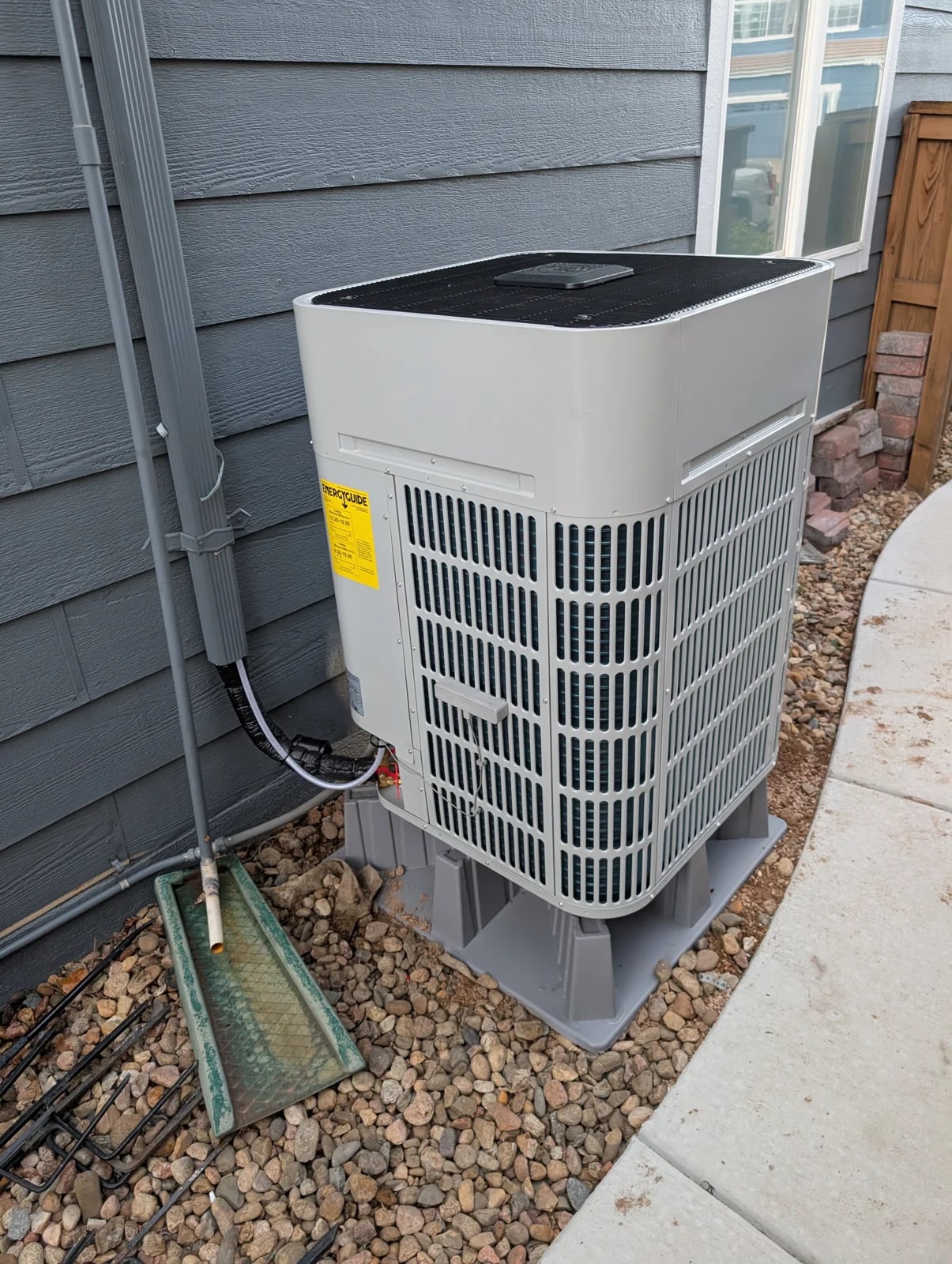 A Bosch outdoor unit on risers in a rock bed beside gray siding, with a covered line route up the wall